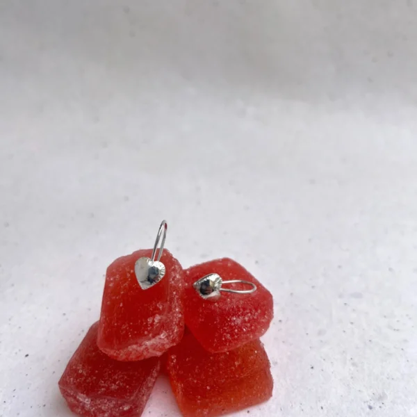 Handmade silver earrings. They feature two tiny hearts all soldered together, with a hook clasp. they are laid on red candy