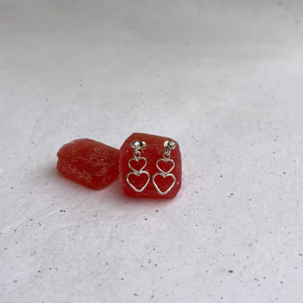 Handmade silver earrings. They feature two tiny hearts all soldered together, with a hook clasp. they are laid on red candy