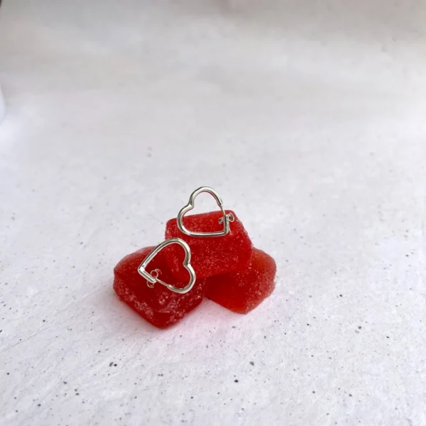 Handmade silver heart shaped earrings, laid on red candy