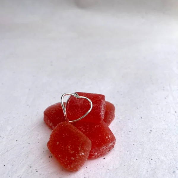 Handmade heart shaped silver ring laid on red coloured candy.