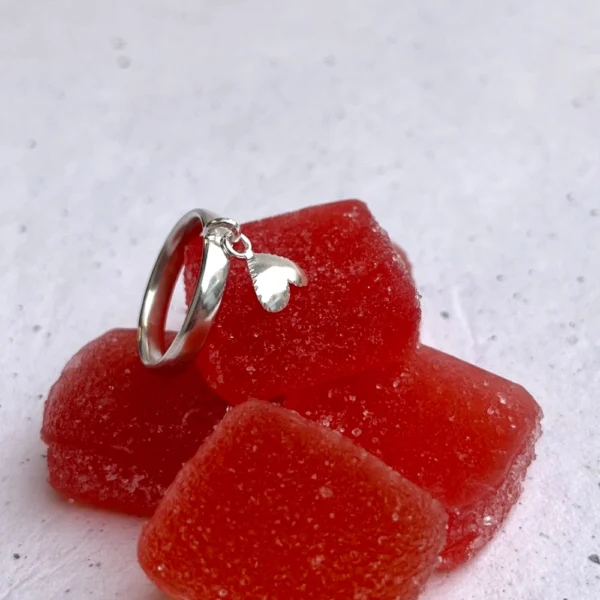Handmade silver ring with a heart shaped element that moves, laid on red coloured candy.