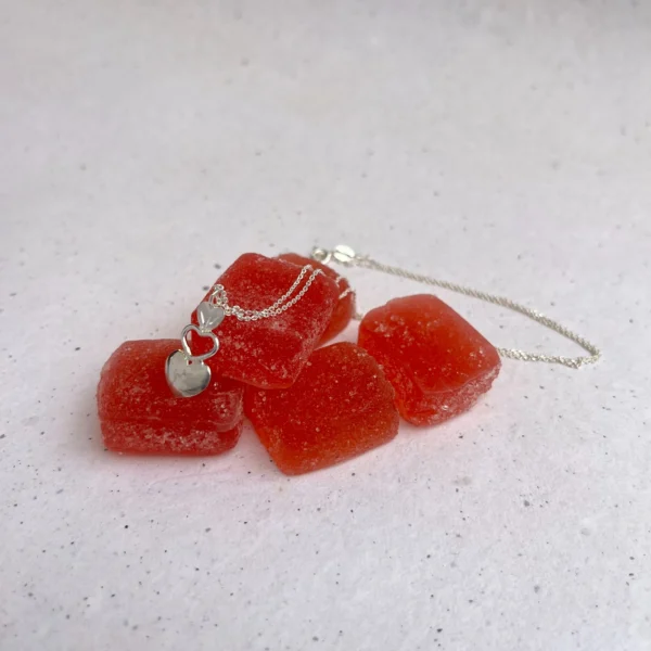 Handmade silver pendant with a triple heart element hanging on a silver chain. the pendant is on red candy.