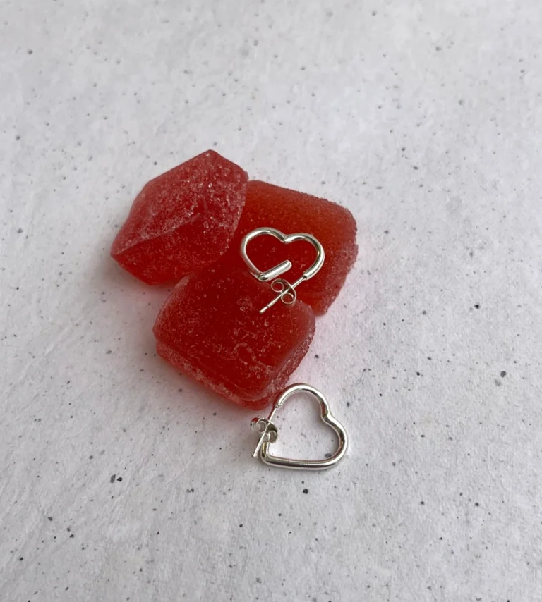 Χειροποίητα, ασημένια σκουλαρίκια σε σχήμα καρδιάς, πάνω σε κόκκινα ζαχαρωτά.