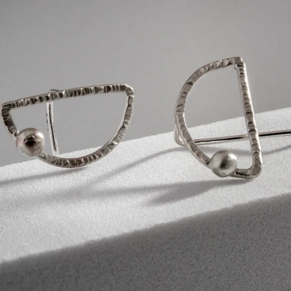 Close up of Maya asymmetrical hammered sterling silver earrings with geometric open shapes and rounded silver details, handmade by Vasiliki Sountou Jewellery.