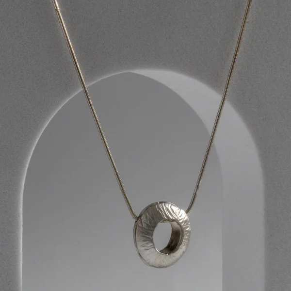 Orbit necklace with a handmade hammered recycled sterling silver pendant featuring a rounded three-dimensional shape, open centre and satin finish by Vasiliki Sountou Jewellery.